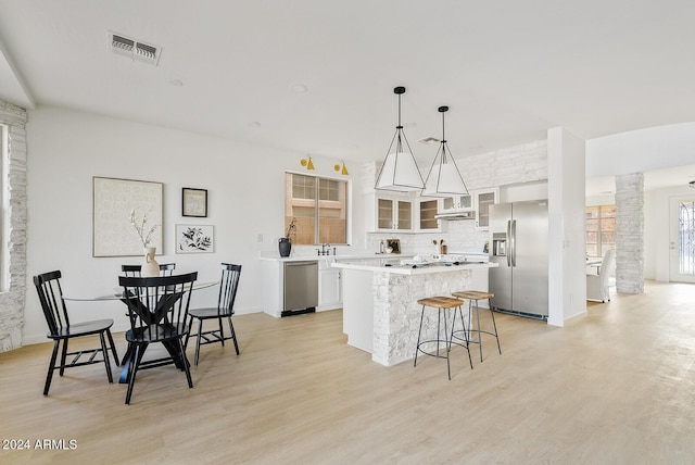 kitchen featuring appliances with stainless steel finishes, pendant lighting, a center island, light hardwood / wood-style floors, and white cabinetry