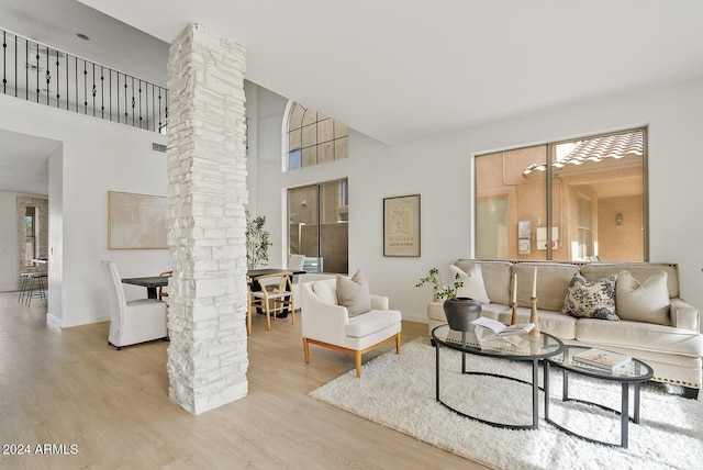 living room with a towering ceiling, light hardwood / wood-style floors, and ornate columns