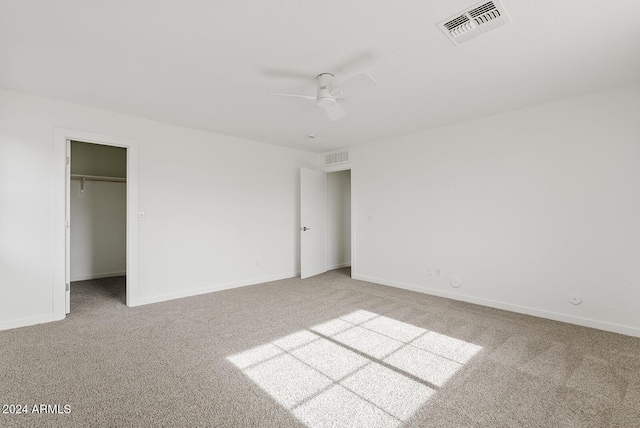 unfurnished bedroom featuring a closet, a spacious closet, ceiling fan, and light colored carpet