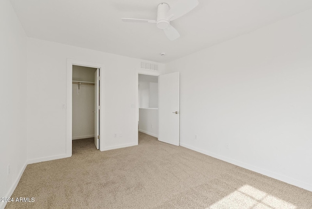 unfurnished bedroom with a walk in closet, ceiling fan, a closet, and light colored carpet