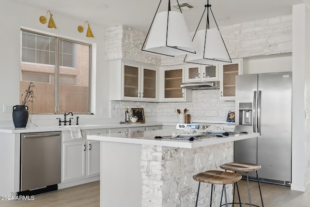 kitchen with light wood-type flooring, stainless steel appliances, pendant lighting, white cabinets, and a breakfast bar area