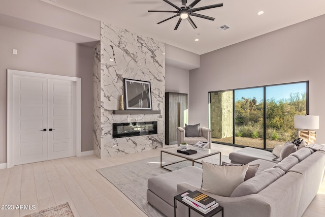 living room with a high ceiling, ceiling fan, a premium fireplace, and light hardwood / wood-style flooring