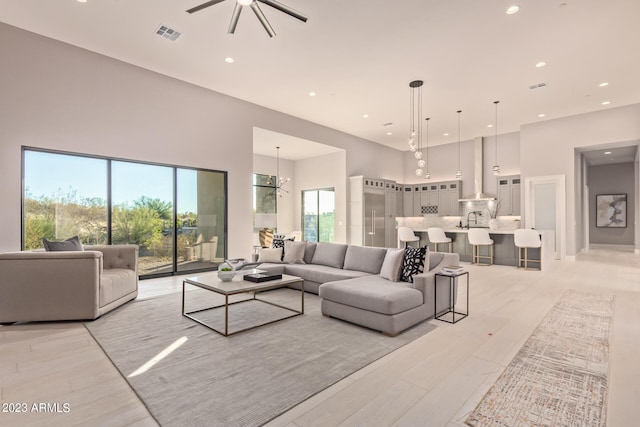 living room with light hardwood / wood-style floors, ceiling fan with notable chandelier, and a towering ceiling