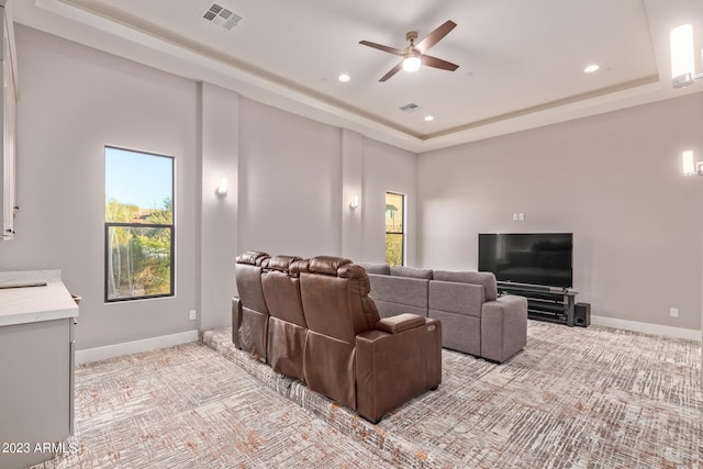 cinema room featuring a tray ceiling, light carpet, and ceiling fan