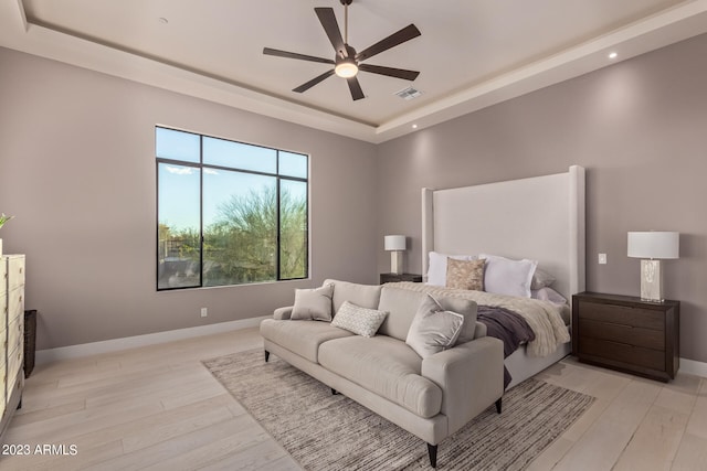 bedroom with light hardwood / wood-style floors, ceiling fan, and a raised ceiling