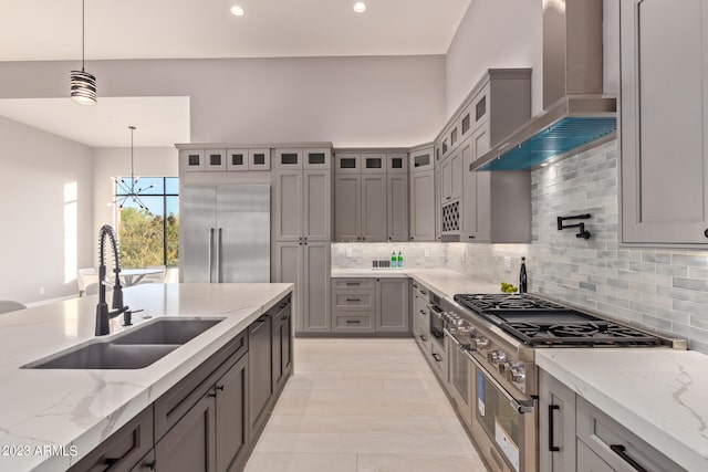 kitchen featuring light stone counters, wall chimney range hood, decorative light fixtures, sink, and high end appliances