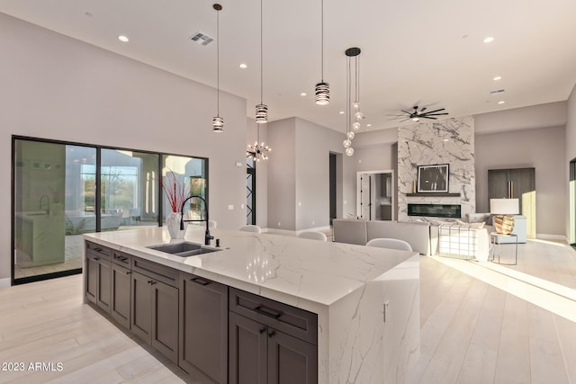 kitchen featuring sink, light stone countertops, hanging light fixtures, an island with sink, and a high end fireplace