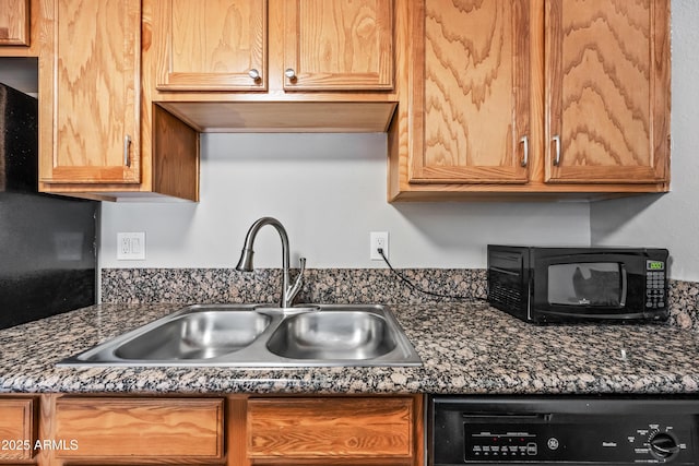 kitchen featuring dishwashing machine, sink, and dark stone counters