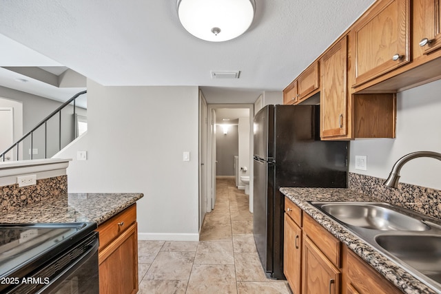 kitchen with black refrigerator, sink, dark stone countertops, and light tile patterned flooring