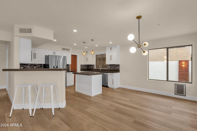 kitchen featuring a center island, white cabinetry, stainless steel appliances, backsplash, and decorative light fixtures