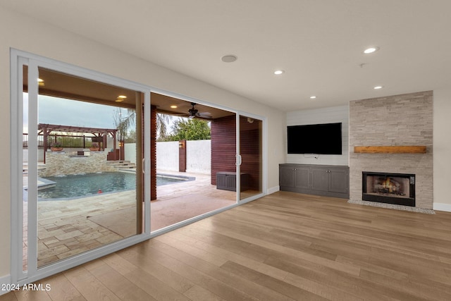 unfurnished living room with ceiling fan, a stone fireplace, and light hardwood / wood-style flooring