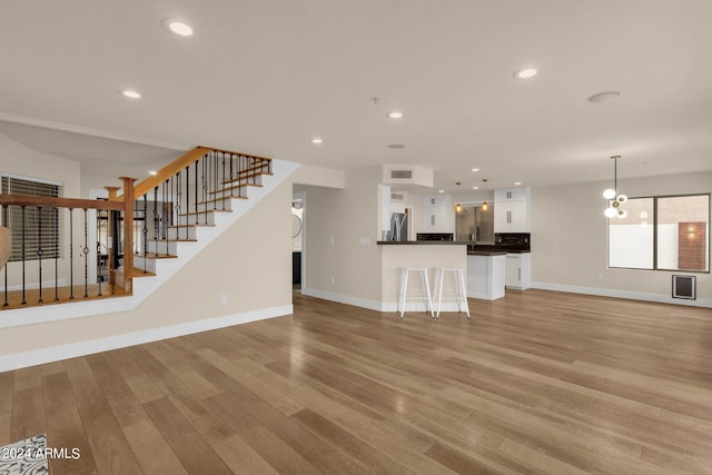 unfurnished living room with an inviting chandelier and light hardwood / wood-style floors