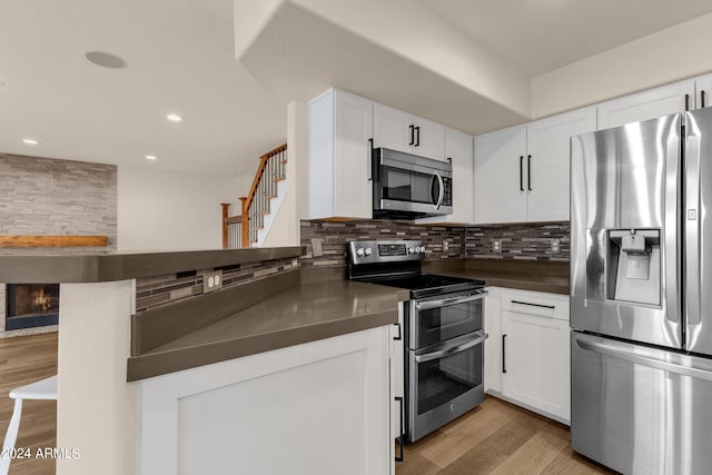 kitchen with light hardwood / wood-style flooring, appliances with stainless steel finishes, kitchen peninsula, and white cabinetry