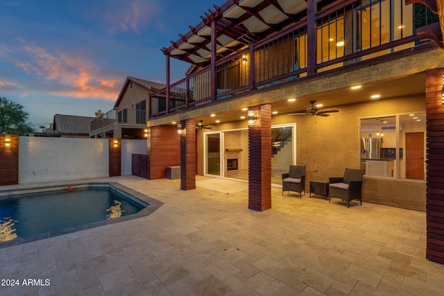 pool at dusk with a patio and ceiling fan