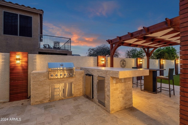 patio terrace at dusk with a balcony, a grill, a pergola, exterior kitchen, and an outdoor bar