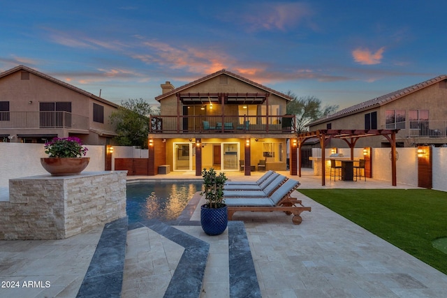 back house at dusk with a patio, a balcony, and a yard