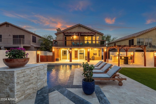 back house at dusk with a balcony, an outdoor living space, and a patio