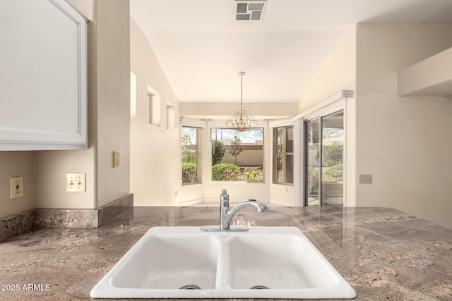 kitchen featuring dark stone countertops, visible vents, lofted ceiling, a sink, and pendant lighting