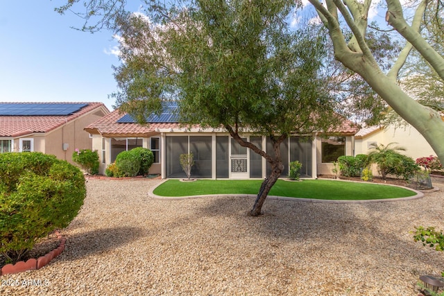 view of front of house featuring stucco siding, a tile roof, a front yard, a sunroom, and solar panels