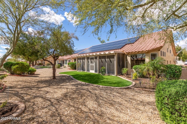 rear view of property with stucco siding, a lawn, a tile roof, a sunroom, and solar panels