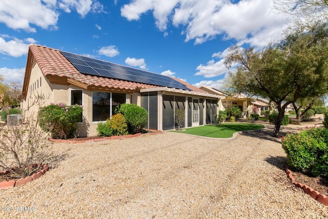 back of house featuring stucco siding, a tiled roof, and solar panels