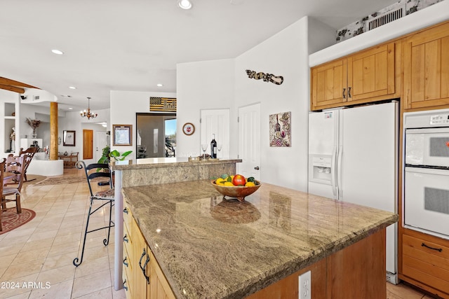 kitchen featuring light tile patterned flooring, a kitchen breakfast bar, white appliances, a kitchen island, and a notable chandelier