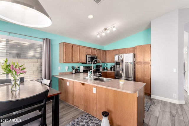 kitchen with vaulted ceiling, sink, kitchen peninsula, stainless steel appliances, and light wood-type flooring