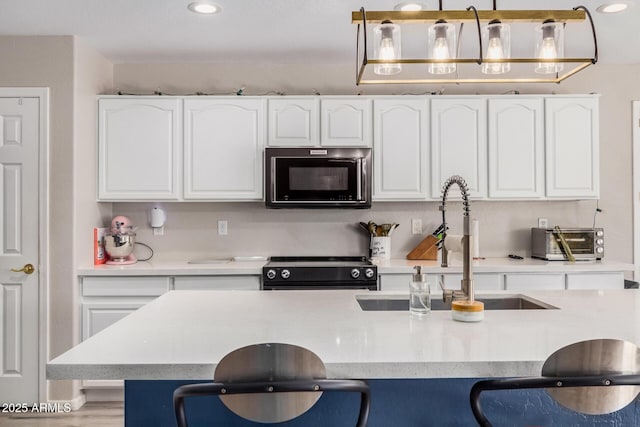 kitchen with white cabinets, a sink, a kitchen bar, and black appliances
