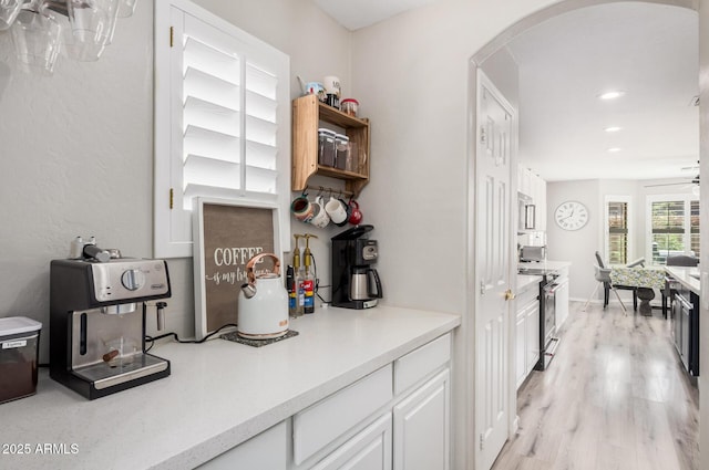 kitchen with white cabinets, arched walkways, light wood-type flooring, light countertops, and high end range