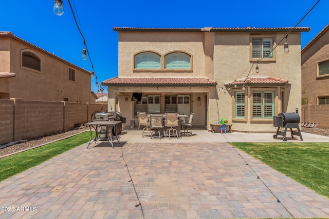 rear view of property featuring a patio area, a fenced backyard, outdoor dining space, and a tiled roof