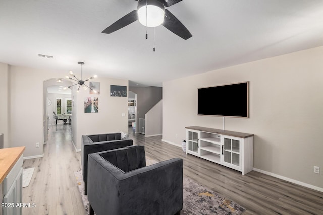 living room featuring arched walkways, light wood finished floors, baseboards, and ceiling fan with notable chandelier