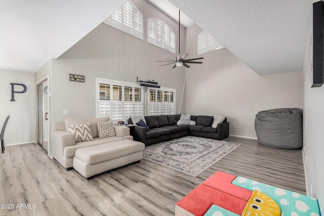 living room featuring ceiling fan, baseboards, a high ceiling, and light wood-style flooring