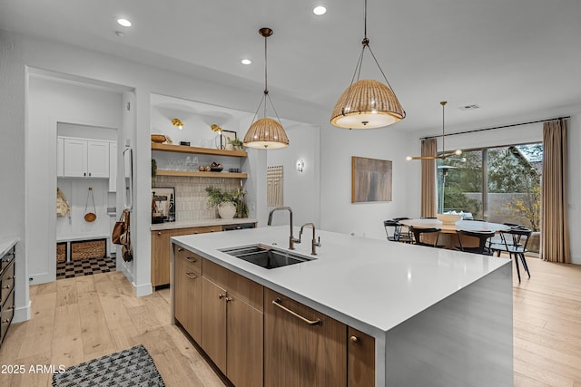 kitchen with pendant lighting, backsplash, a kitchen island with sink, sink, and light hardwood / wood-style floors