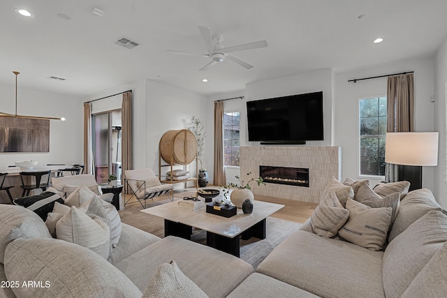 living room featuring a tile fireplace, light hardwood / wood-style floors, and ceiling fan