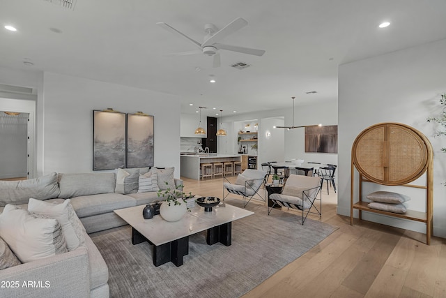 living room with light wood-type flooring, ceiling fan, and sink