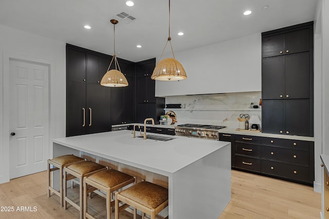 kitchen with sink, pendant lighting, a kitchen bar, a kitchen island with sink, and high end range