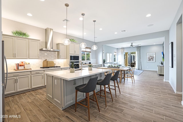 kitchen with stainless steel gas stovetop, an island with sink, a kitchen bar, hanging light fixtures, and wall chimney exhaust hood