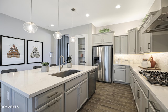 kitchen with gray cabinets, appliances with stainless steel finishes, decorative light fixtures, sink, and wall chimney exhaust hood