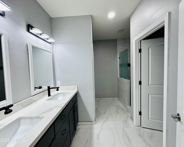 bathroom featuring marble finish floor, a tile shower, a sink, and double vanity