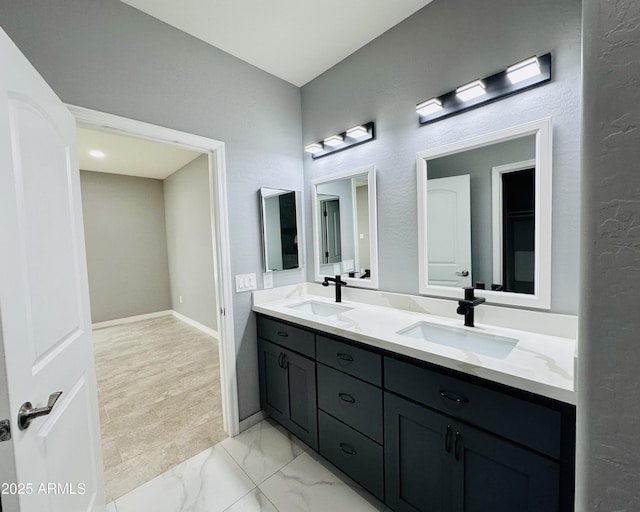 full bathroom with marble finish floor, baseboards, a sink, and double vanity