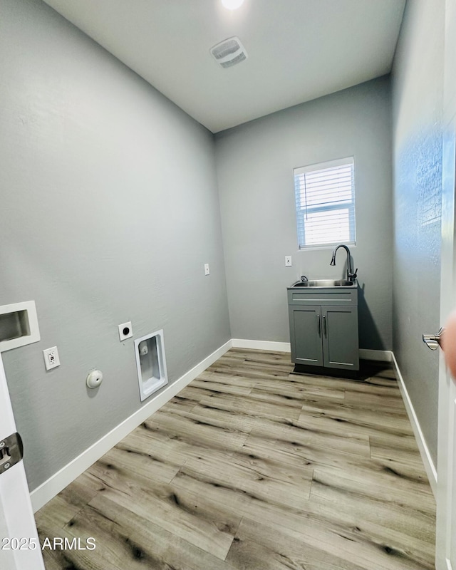 laundry area featuring a sink, hookup for an electric dryer, cabinet space, light wood-style flooring, and hookup for a gas dryer