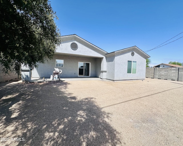 rear view of house featuring stucco siding, fence, and a patio