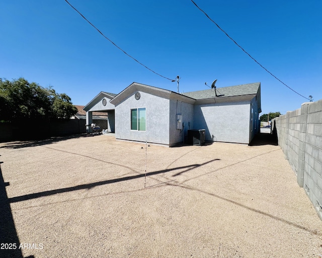 back of house featuring fence, central AC unit, and stucco siding