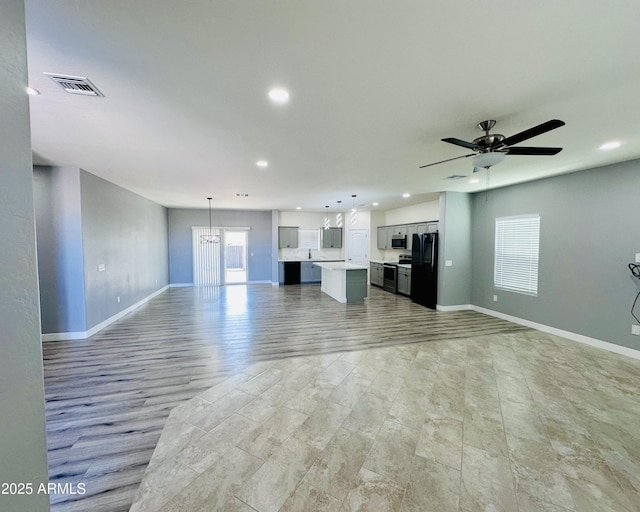 unfurnished living room featuring recessed lighting, visible vents, baseboards, and ceiling fan with notable chandelier