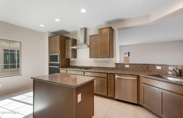 kitchen featuring wall chimney range hood, dark stone counters, a kitchen island, light tile patterned floors, and stainless steel appliances