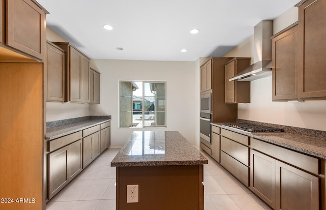 kitchen with light tile patterned floors, appliances with stainless steel finishes, wall chimney exhaust hood, and a kitchen island