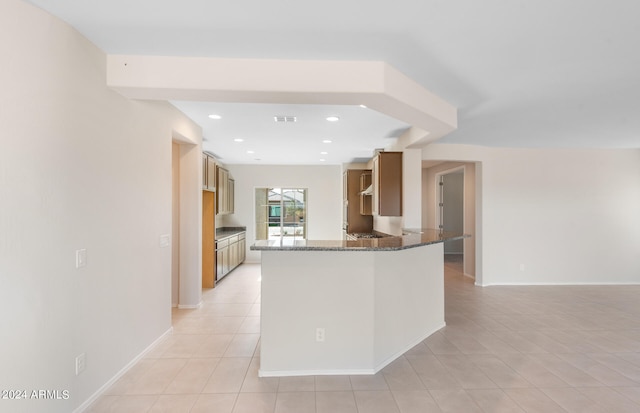 kitchen featuring light tile patterned floors, kitchen peninsula, and dark stone counters