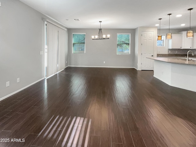 unfurnished living room featuring sink, dark hardwood / wood-style floors, and an inviting chandelier