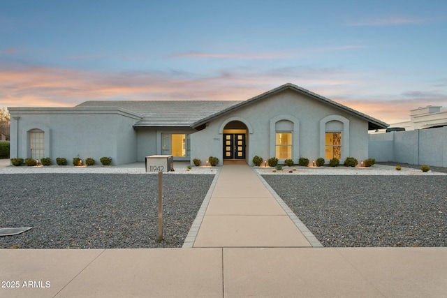 view of front facade with fence private yard, french doors, and stucco siding