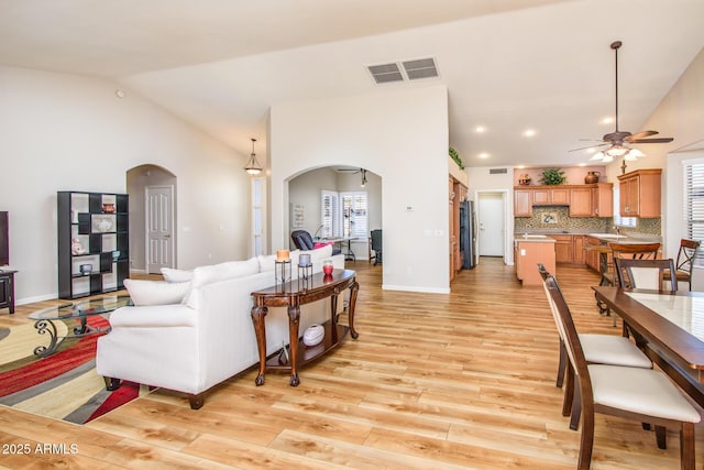 living area featuring arched walkways, light wood-style floors, visible vents, and a ceiling fan